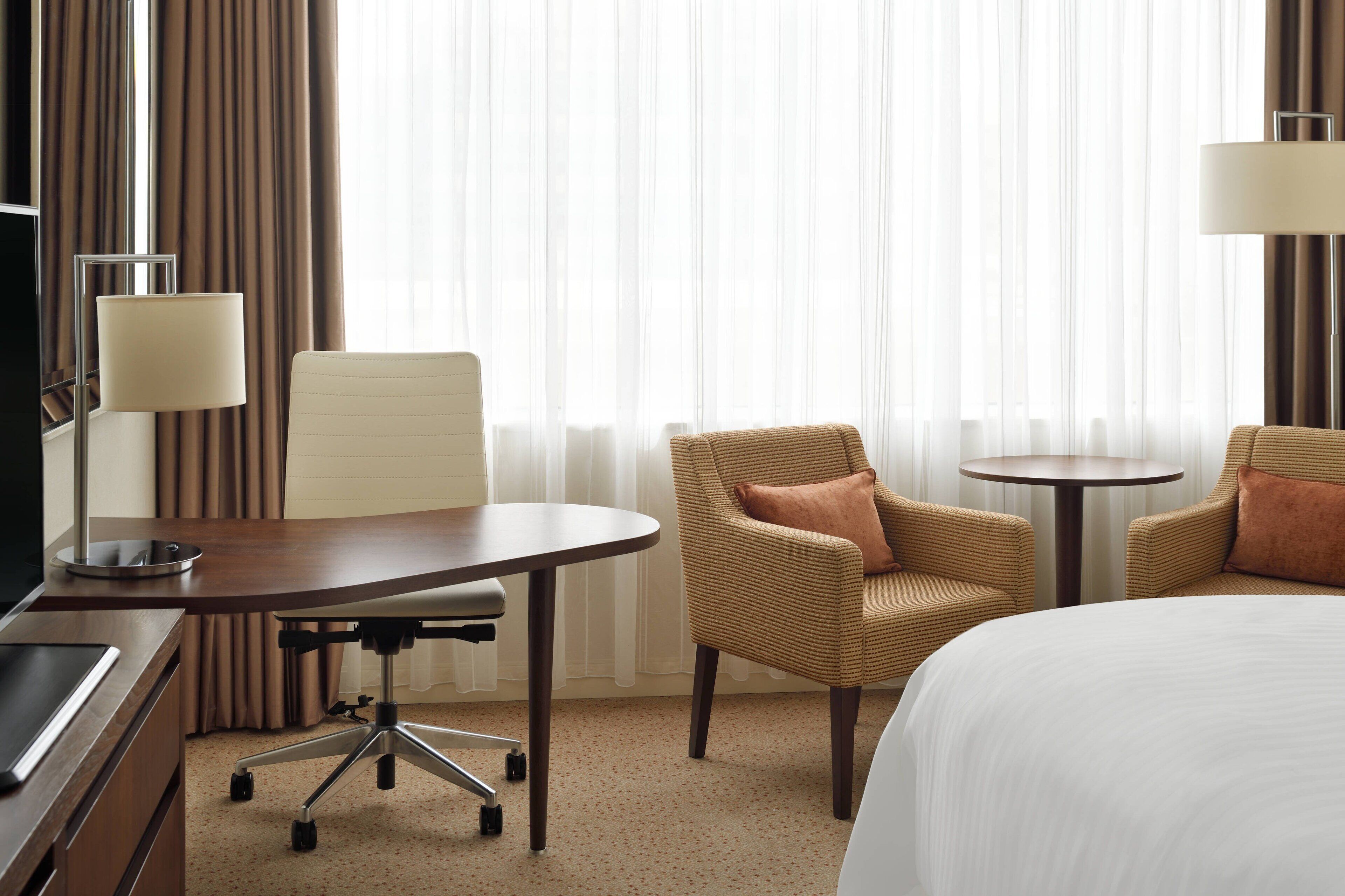 Una habitación de hotel con cama, escritorio con lámpara, dos sillones y una mesita.