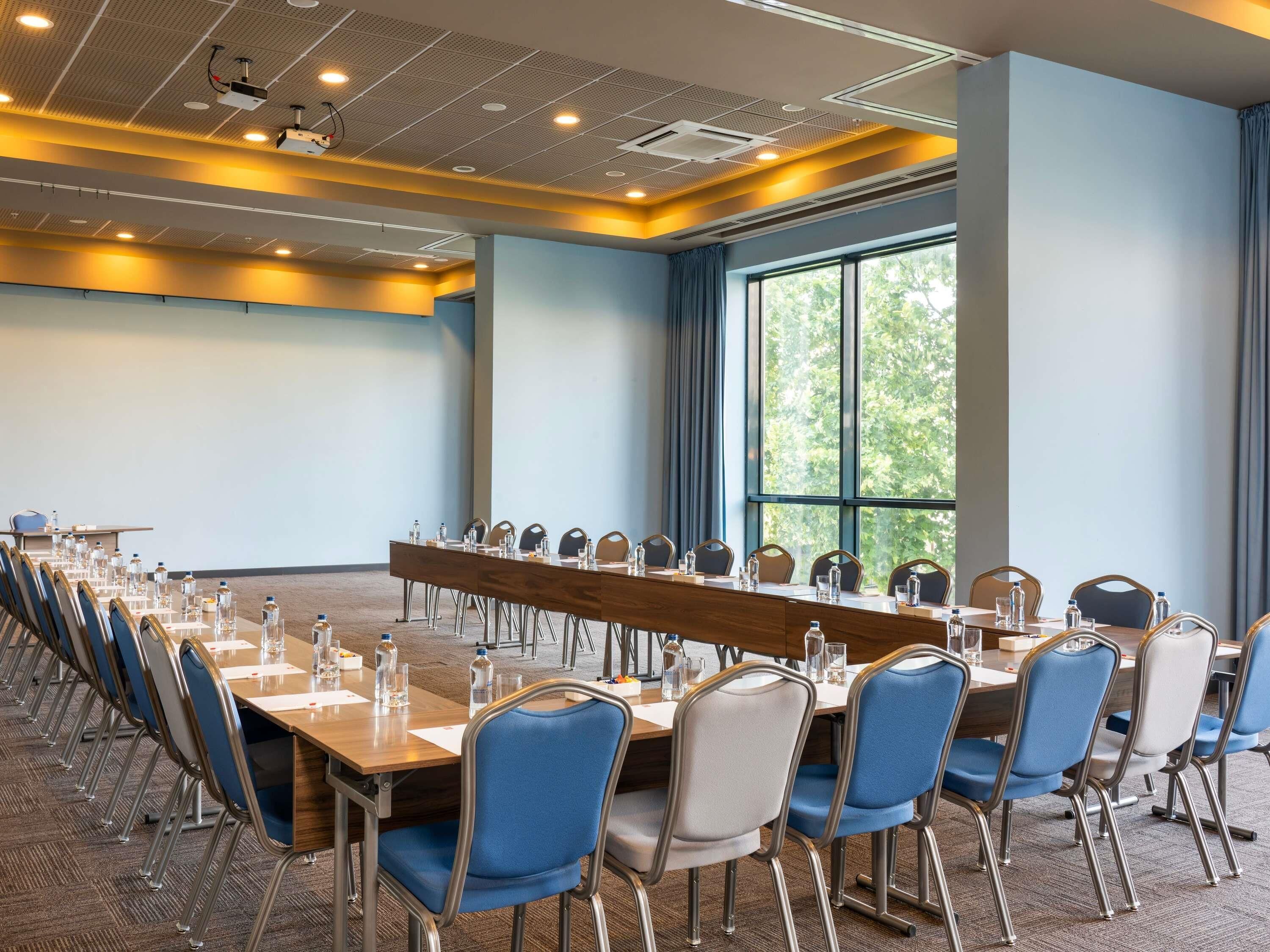 A conference room with a long table, blue chairs, and a large window with a view of trees.