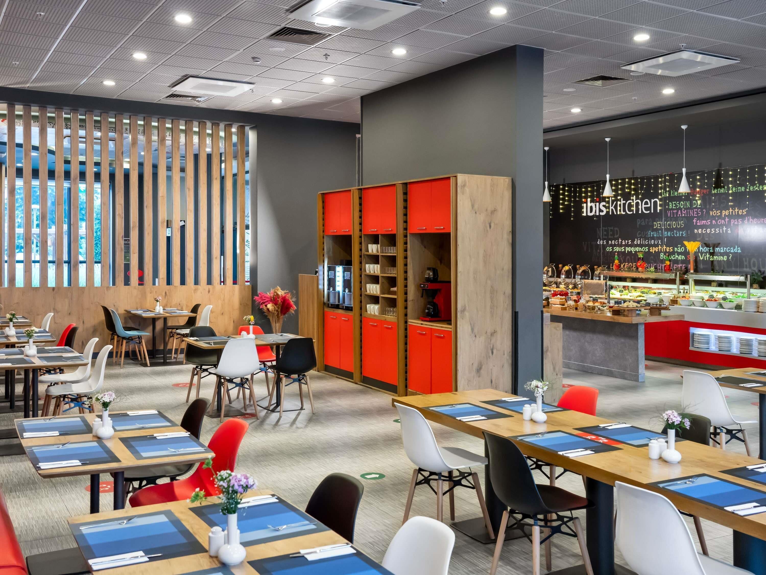 A modern restaurant interior with multiple dining tables, red cabinets, and a visible kitchen area.