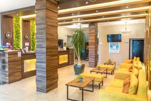 Eine Hotelhalle mit einer Rezeption, einer Sitzecke und einer großen Pflanze in einem Topf.
