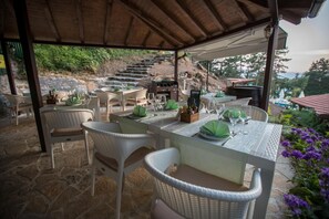 Un área de comedor al aire libre con sillas y mesas de mimbre, piso de piedra y vista a una escalera que sube.