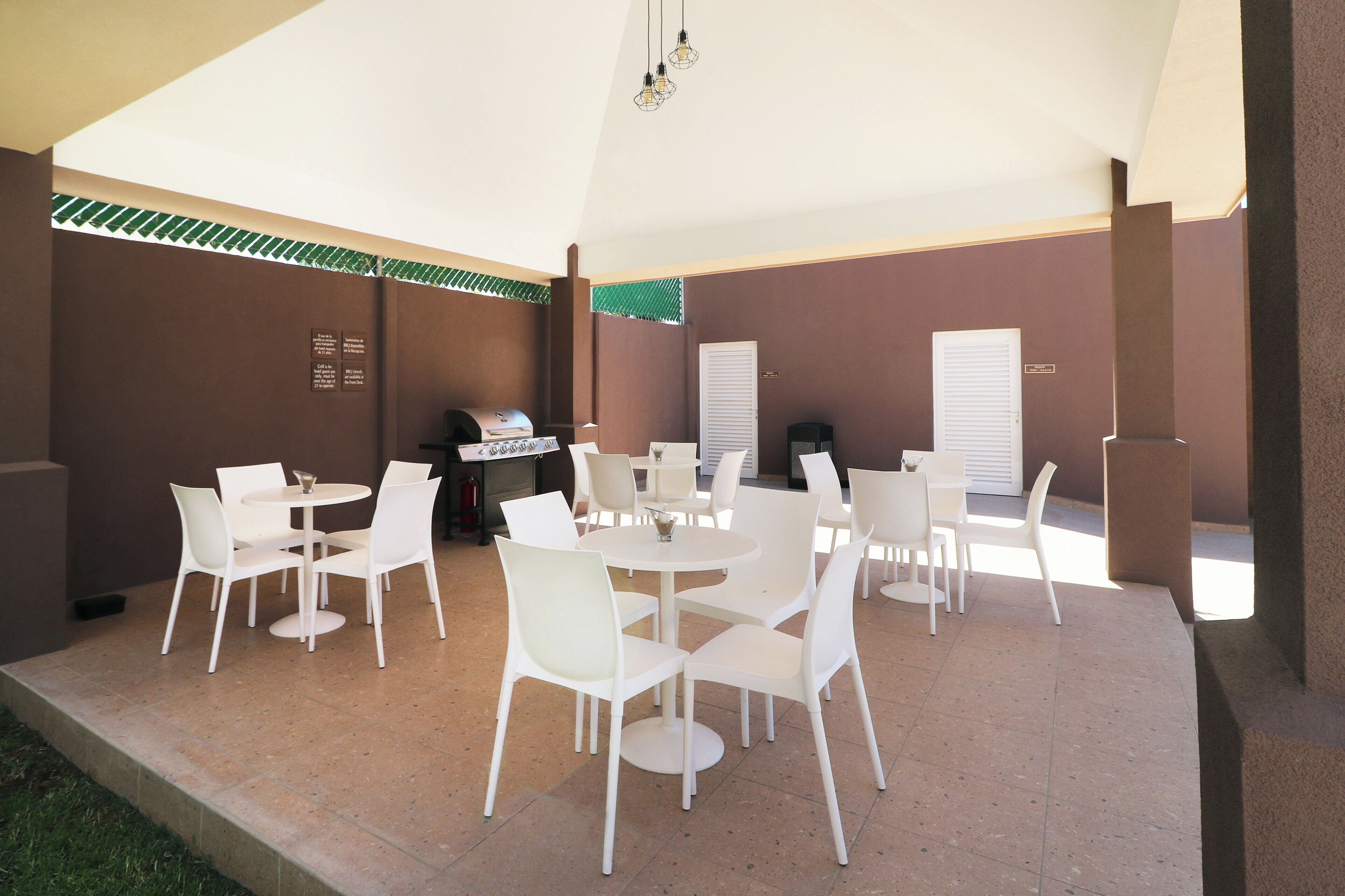 Eine Terrasse im Freien mit weißen Tischen und Stühlen, einem Grill und einem überdachten Bereich.