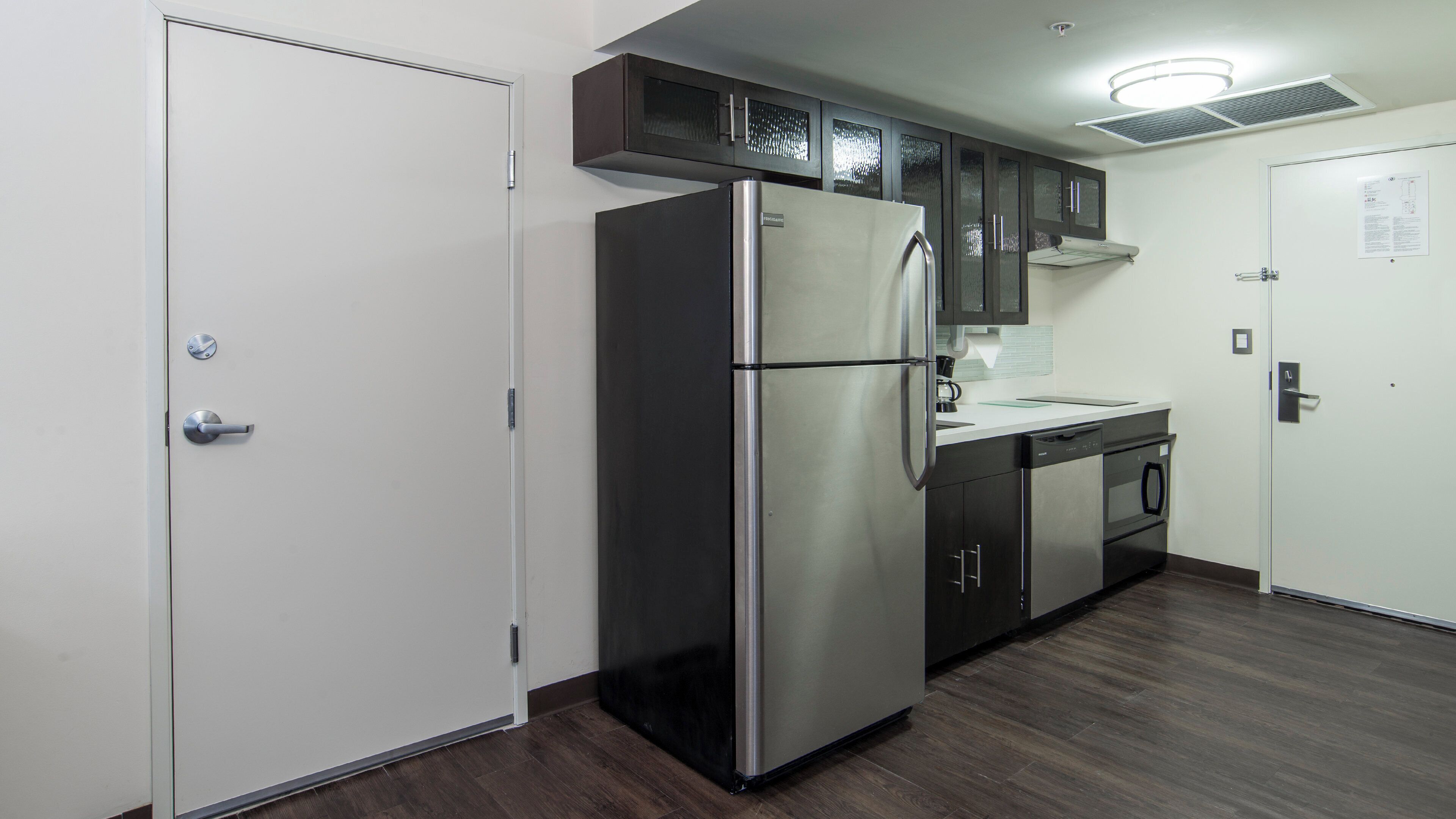 A kitchen with a stainless steel refrigerator, dark wooden cabinets, and a white countertop.