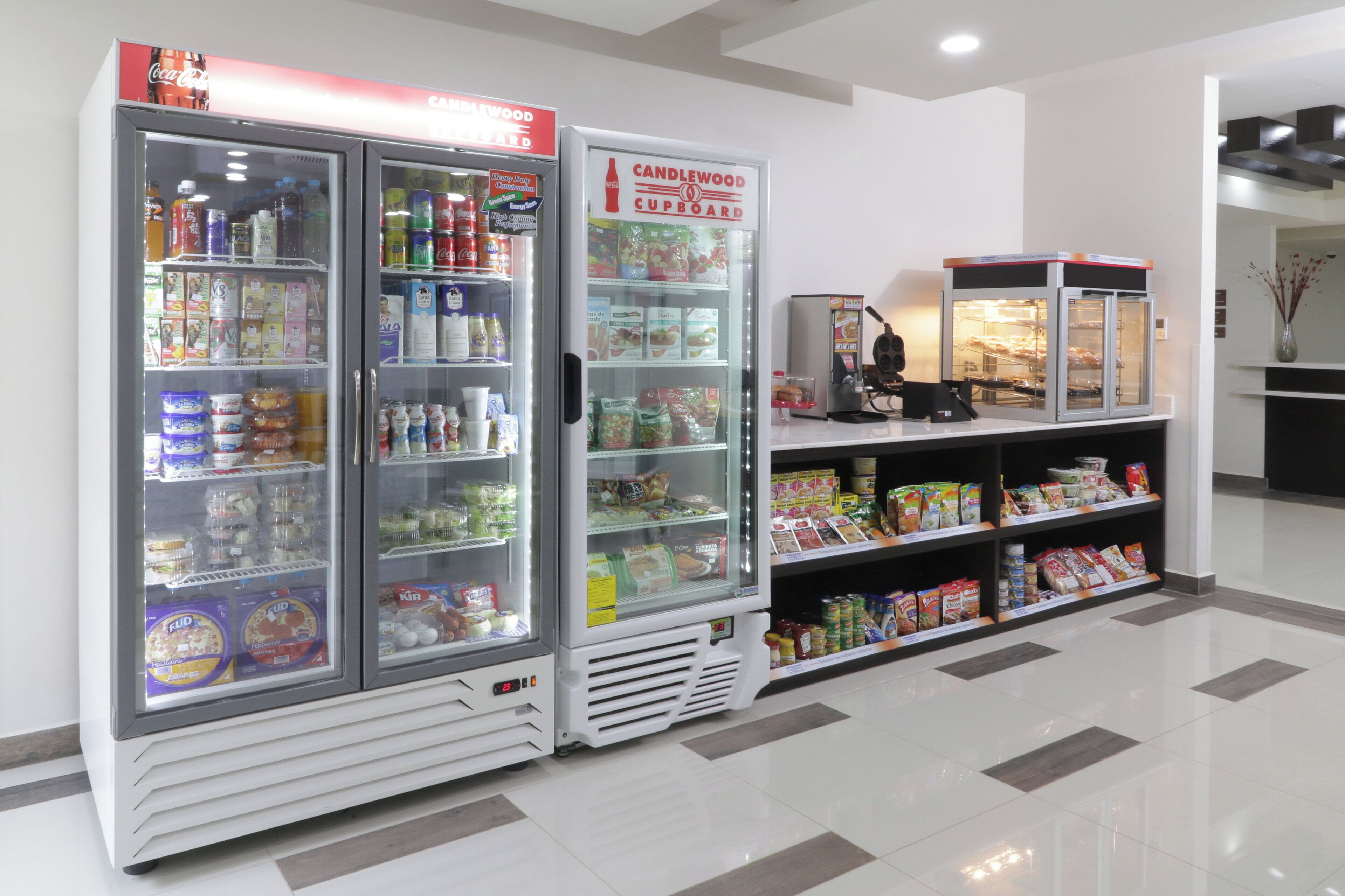 Un patio de comidas limpio y bien iluminado, con dispensadores de bebidas refrigeradas y estantes llenos de bocadillos y bebidas.