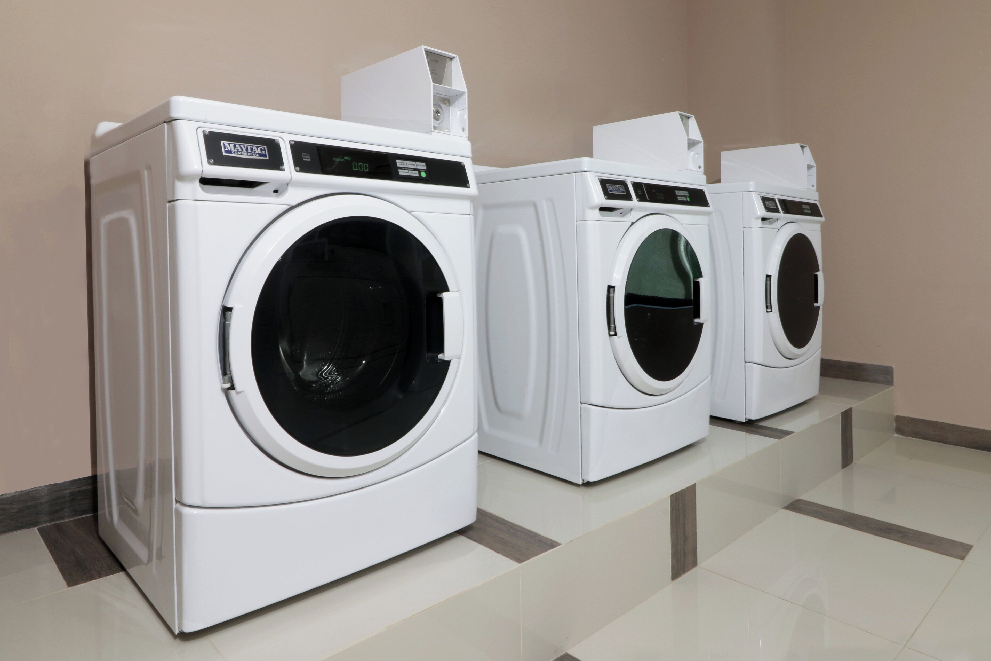 A row of white commercial washing machines in a clean, tiled room.