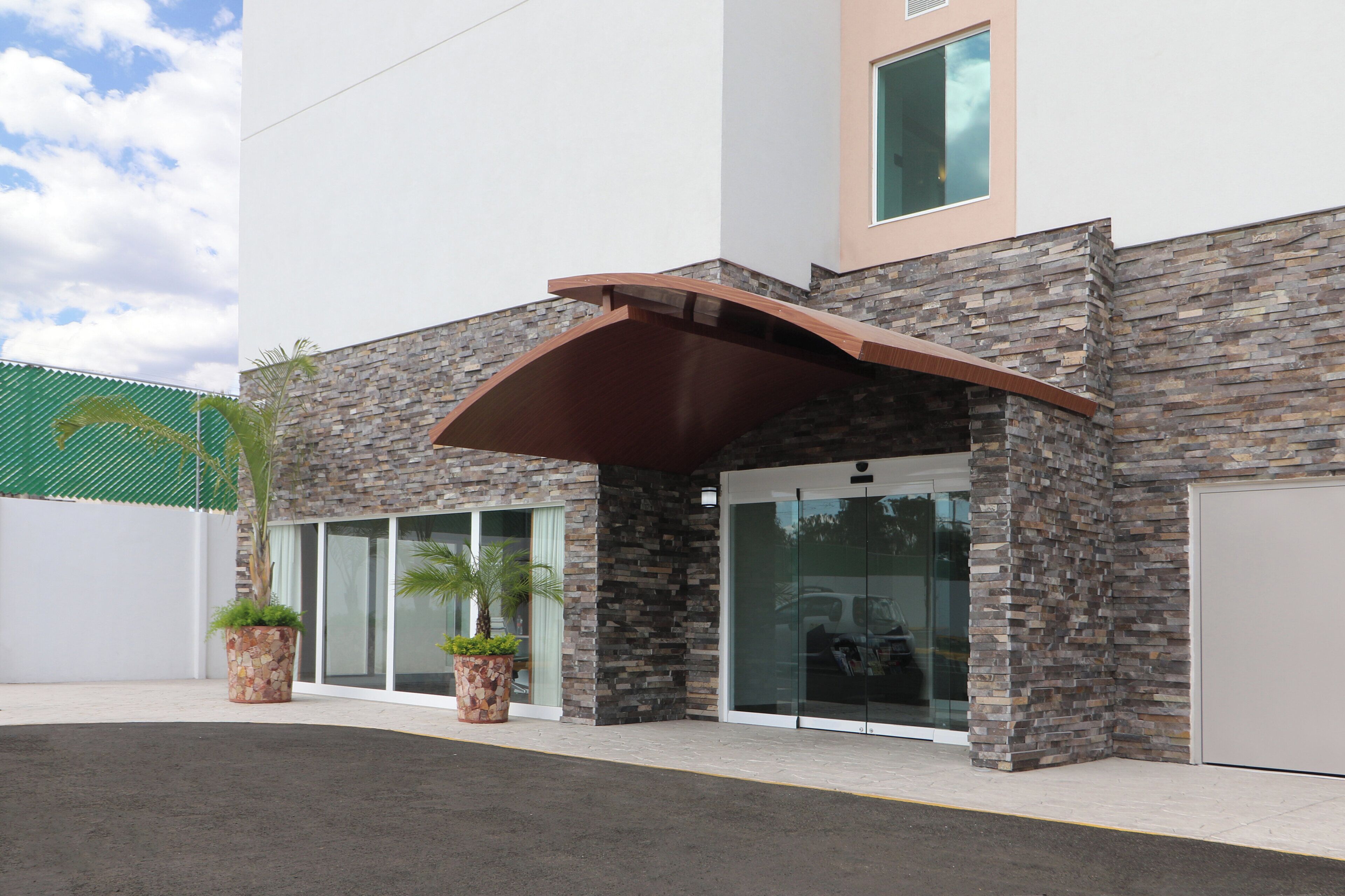 Un edificio moderno con fachada de piedra, puertas de cristal grandes y un acceso cubierto.