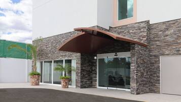 Un edificio moderno con fachada de piedra, puertas de cristal grandes y un acceso cubierto.