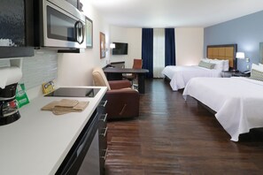 Ein Hotelzimmer mit Küchenzeile, zwei Betten, einem Schreibtisch und einem Fernseher.