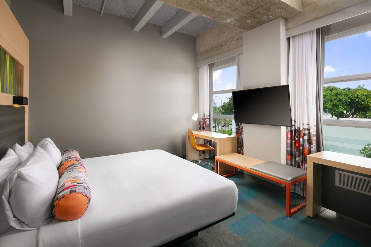 Een hotelkamer met een bed, een bureau, een stoel, een televisie en een raam met uitzicht op bomen.