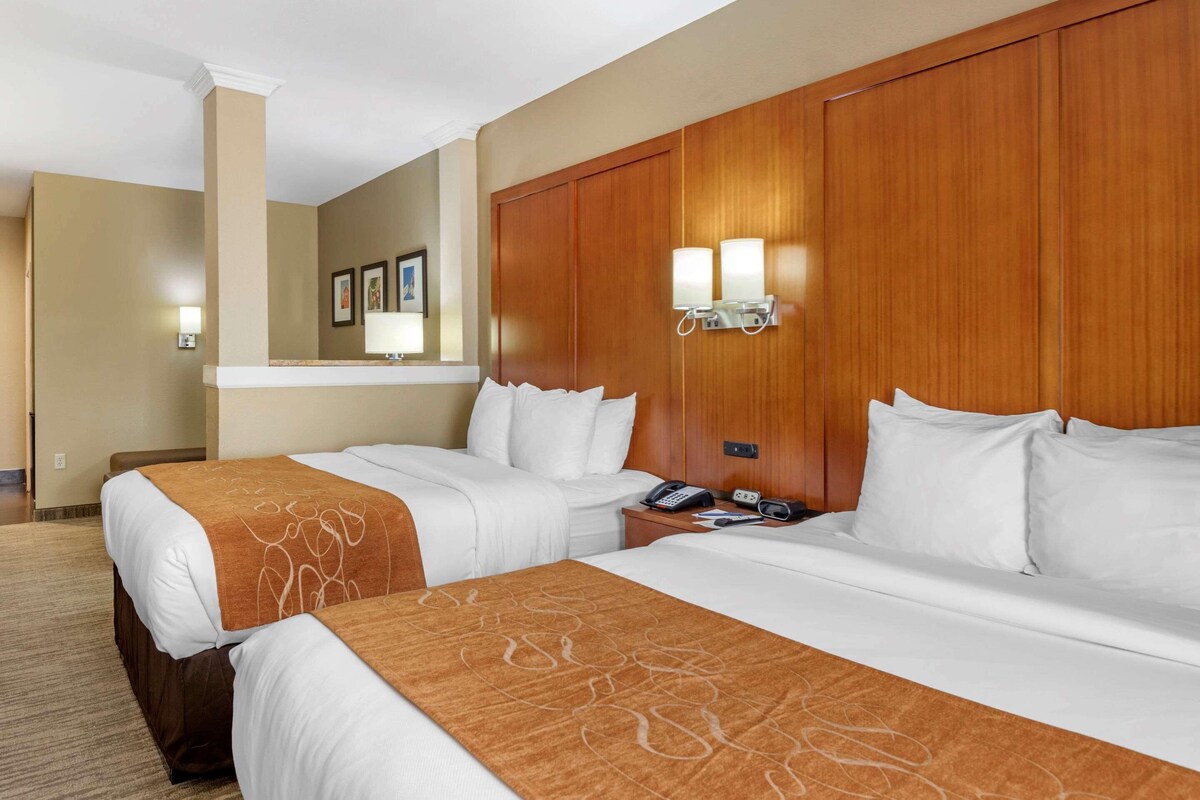 A hotel room with two beds, a wooden headboard, a nightstand with a phone, and wall-mounted lights.