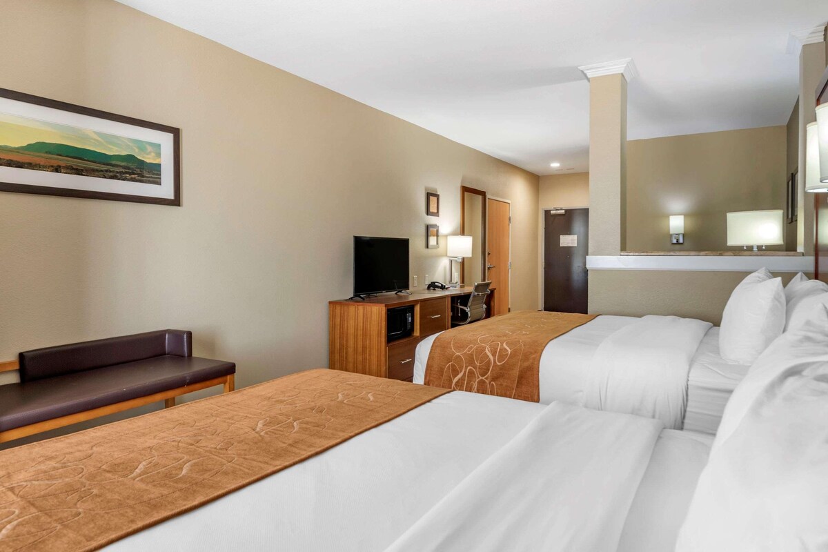 A hotel room with two beds, a desk, a TV, and a painting on the wall.