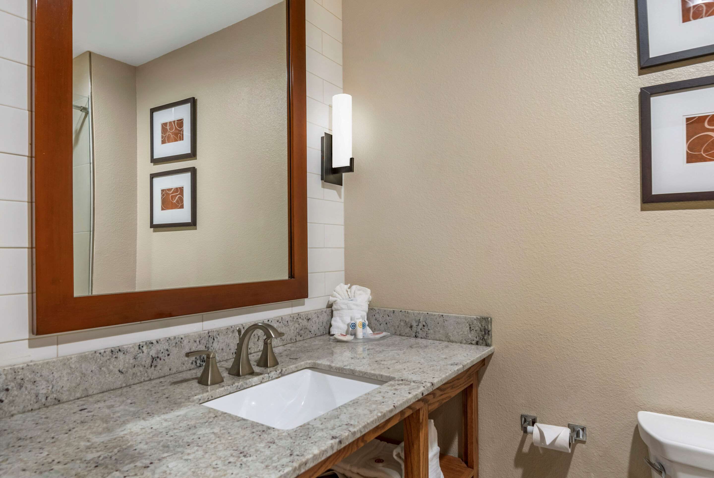 Un baño con un espejo grande, un lavabo, un perchero para toallas y cuadros en la pared.