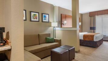 A hotel room with a sofa, ottoman, bed, and artwork on the wall.
