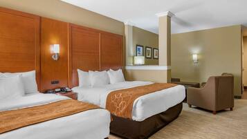 A hotel room with two beds, a wooden headboard, a brown accent wall, and a brown armchair.