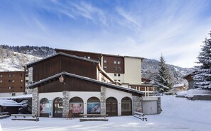 A building with multiple windows and a stone facade, surrounded by snow-covered trees and a clear sky.