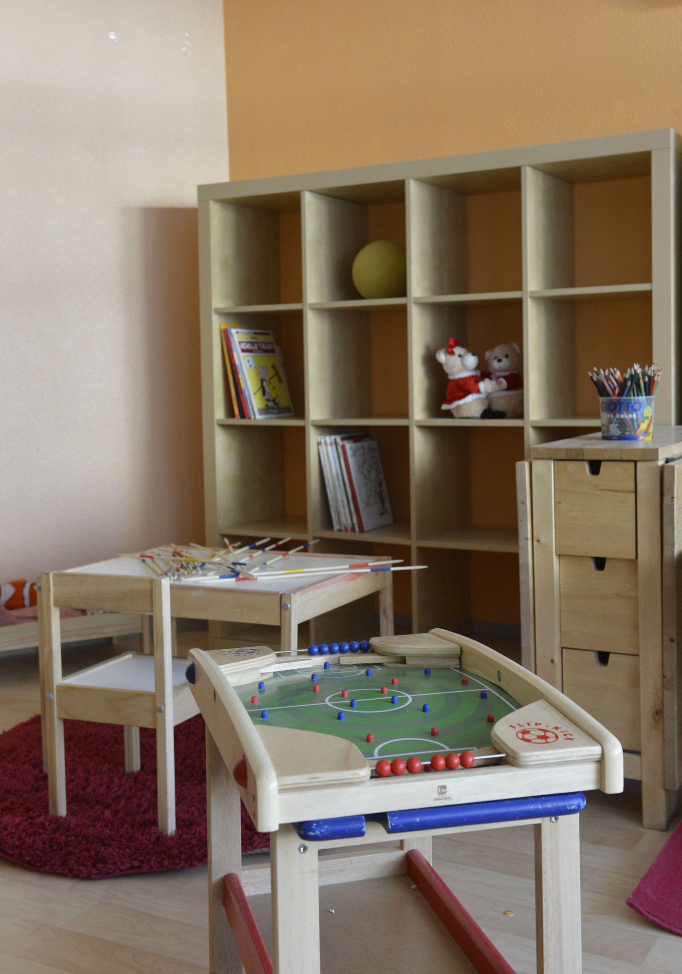 A room with a foosball table, a bookshelf with books and toys, and a desk with art supplies.