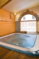 A sauna room with a wooden floor, a stone wall, and a large window with curtains.