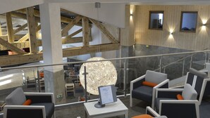 Un hall d’entrée moderne avec un plafond haut, des poutres en bois et une balustrade en verre donnant sur un niveau inférieur.