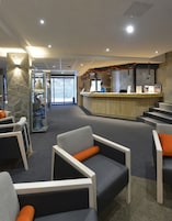 A reception area with a wooden counter, seating with orange cushions, and a stone wall.