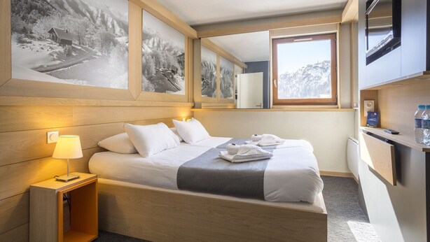 Une chambre d’hôtel avec un lit, une lampe de chevet, un miroir, une fenêtre et un téléviseur fixé au mur.