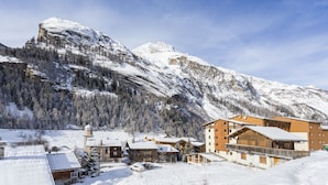Un chalet de montagne composé de plusieurs bâtiments, un paysage enneigé et une montagne imposante en arrière-plan.