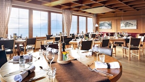 A restaurant with round tables, wooden flooring, and large windows offering mountain views. - Frieden (Pill)