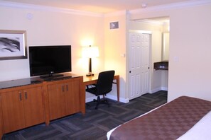 Ett hotellrum med en säng, ett skrivbord med en dator, en tv och en lampa.