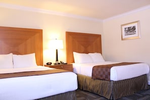 Habitación de hotel con dos camas, una mesita de noche con lámpara y un cuadro en la pared.