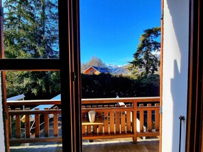 Un pontile in legno con una panchina, un parapetto e vista su una montagna e una casa sullo sfondo.