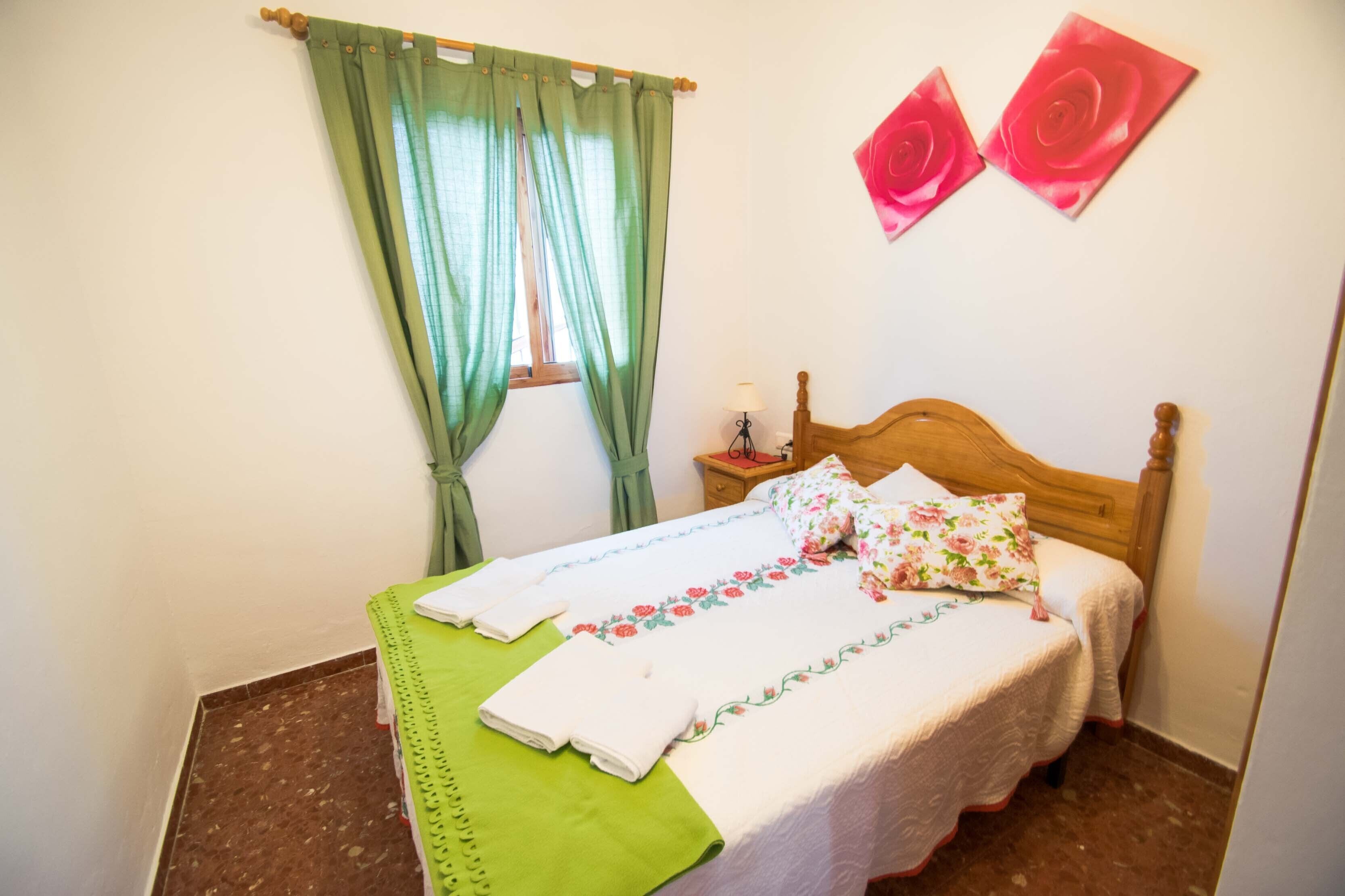 Ein ordentlich bezogenes Bett mit floralen Kissen, einer grünen Tagesdecke und einem Holzkopfstück.