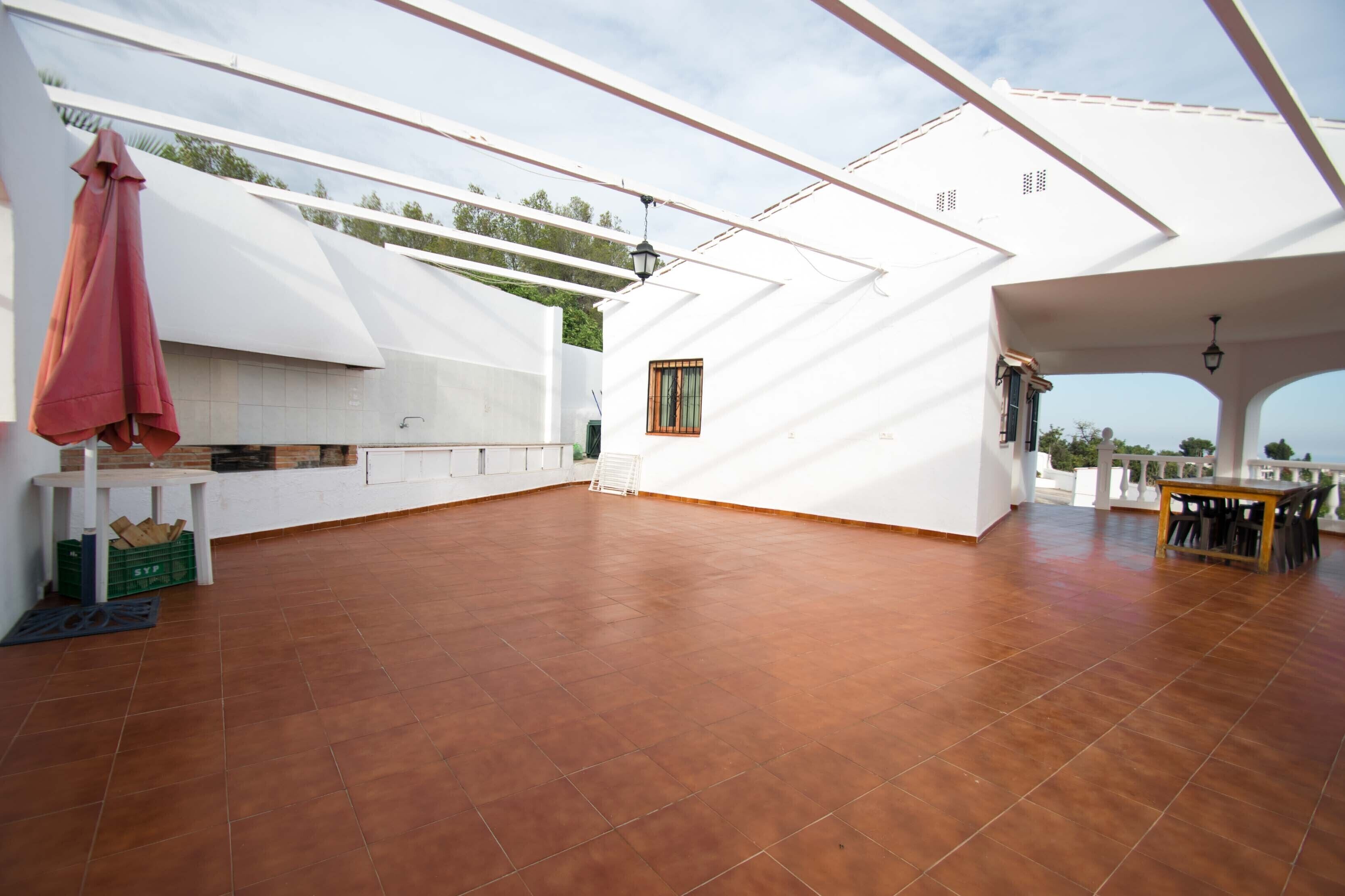 Una terraza espaciosa con suelo de baldosas, una mesa con sillas y una lámpara colgante.