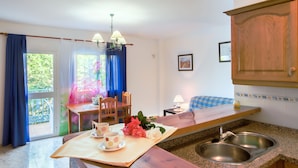 A kitchen with a wooden table, two chairs, a sink, and a window with curtains. - Conjunto Rural Las Rosas (Frigiliana)