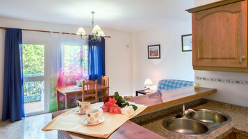 Una cocina con una mesa de madera, dos sillas, un lavabo y un ventanal con cortinas.