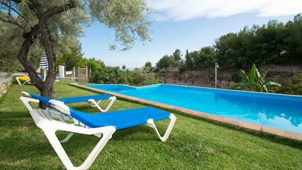 A swimming pool with blue water, surrounded by a grassy area and trees. - Conjunto Rural Las Rosas (Frigiliana)