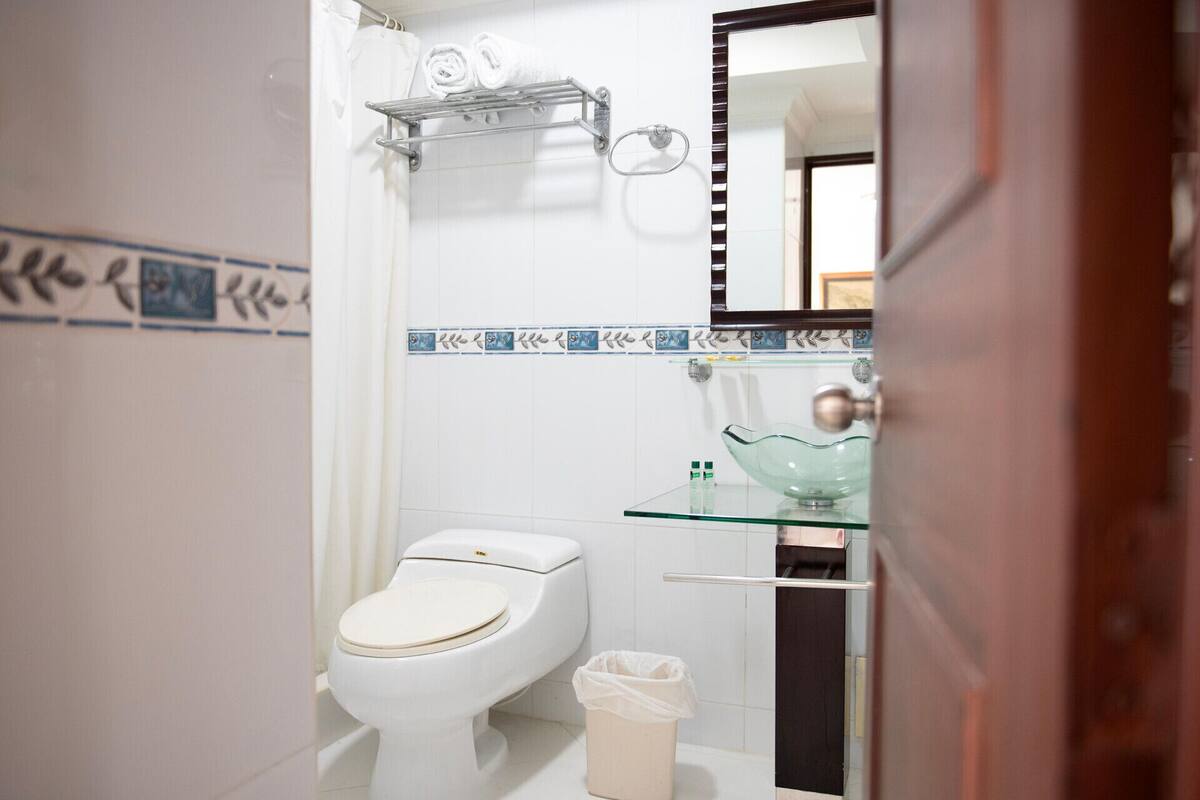 Un baño con inodoro, lavabo de vidrio y un perchero para toallas.