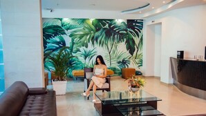 A modern lobby with a large tropical leaf mural, a reception desk, and a seating area with a glass table.