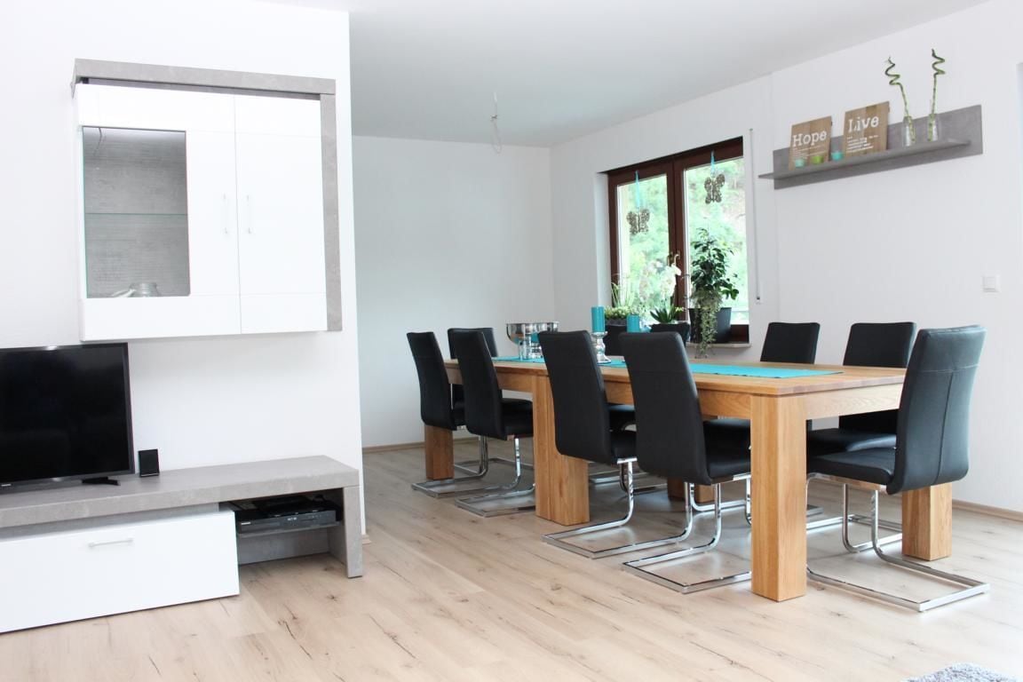 Un comedor moderno con una mesa de madera y sillas negras, un televisor de pantalla plana y un mueble empotrado.