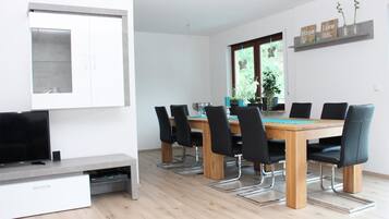 Un comedor moderno con una mesa de madera y sillas negras, un televisor de pantalla plana y un mueble empotrado.
