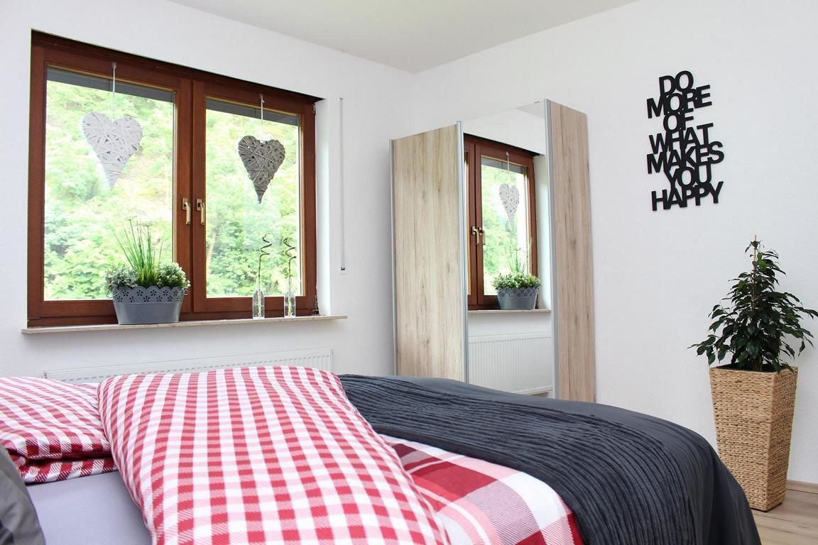 A bedroom with a bed, checkered bedding, a mirror, a potted plant, and a motivational wall quote.