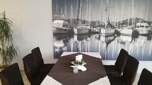 A dining area with a table set for four, a large framed photograph of a marina, and a potted plant to the left. - Centrum Galion (Gda?sk)