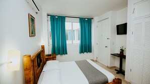 A bedroom with a wooden bed, teal curtains, a TV on the wall, and a small table with a plant. - Hotel NG (Cartagena)