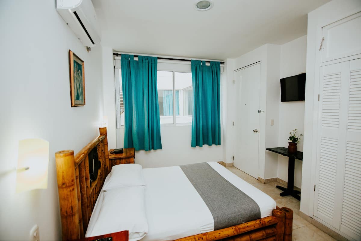 A bedroom with a wooden bed, teal curtains, a TV on the wall, and a small table with a plant.