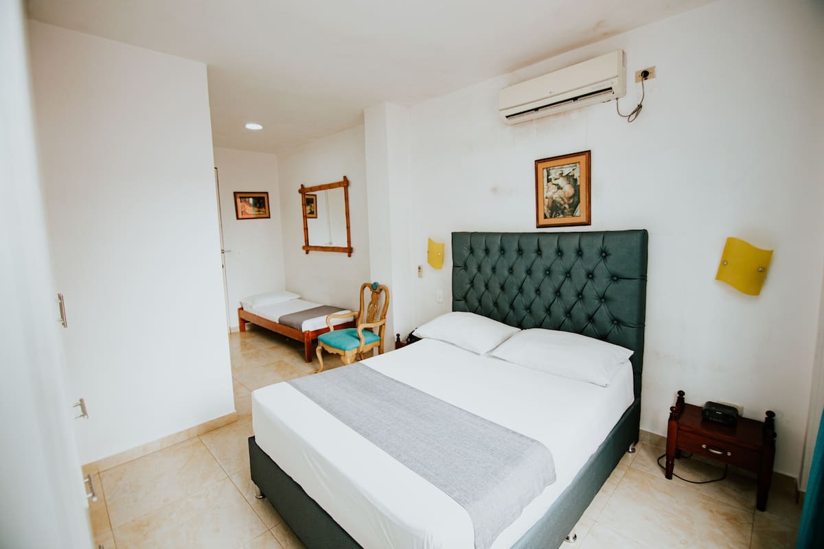 A bedroom with a large bed, a chair, a bedside table, and an air conditioning unit.