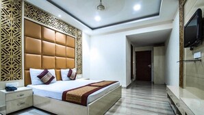 A modern hotel room with a large bed, a bedside table, a TV mounted on the wall, and a patterned wall design. - Orchid Garden (New Delhi)