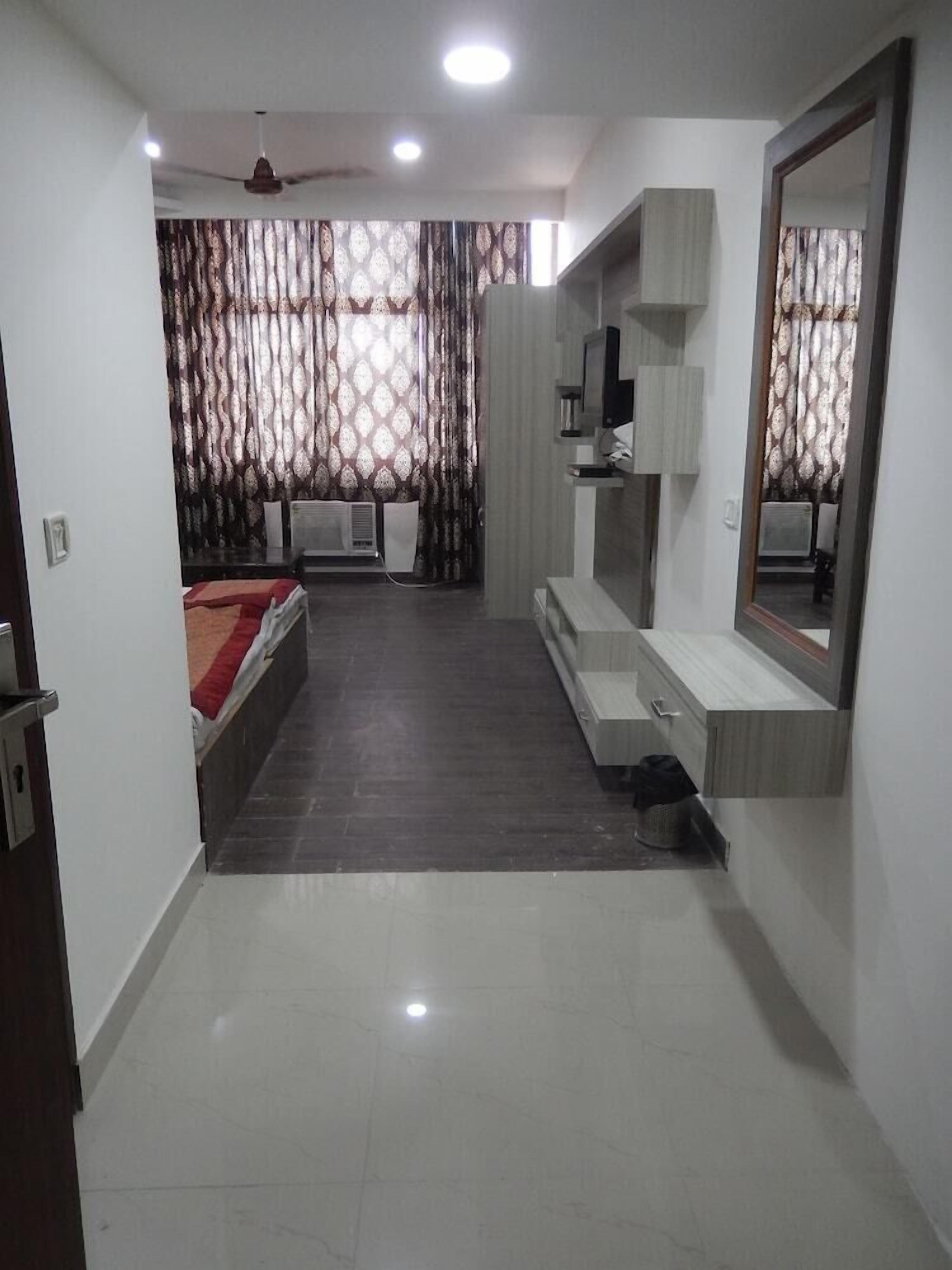 Une chambre à coucher moderne, avec un lit, une coiffeuse dotée d’un miroir, un ventilateur de plafond et des rideaux à motifs.