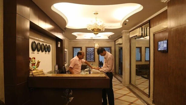 A reception desk labeled 'Orchid Garden' with a chandelier, a travel desk, and a wall with framed items. - Orchid Garden (New Delhi)