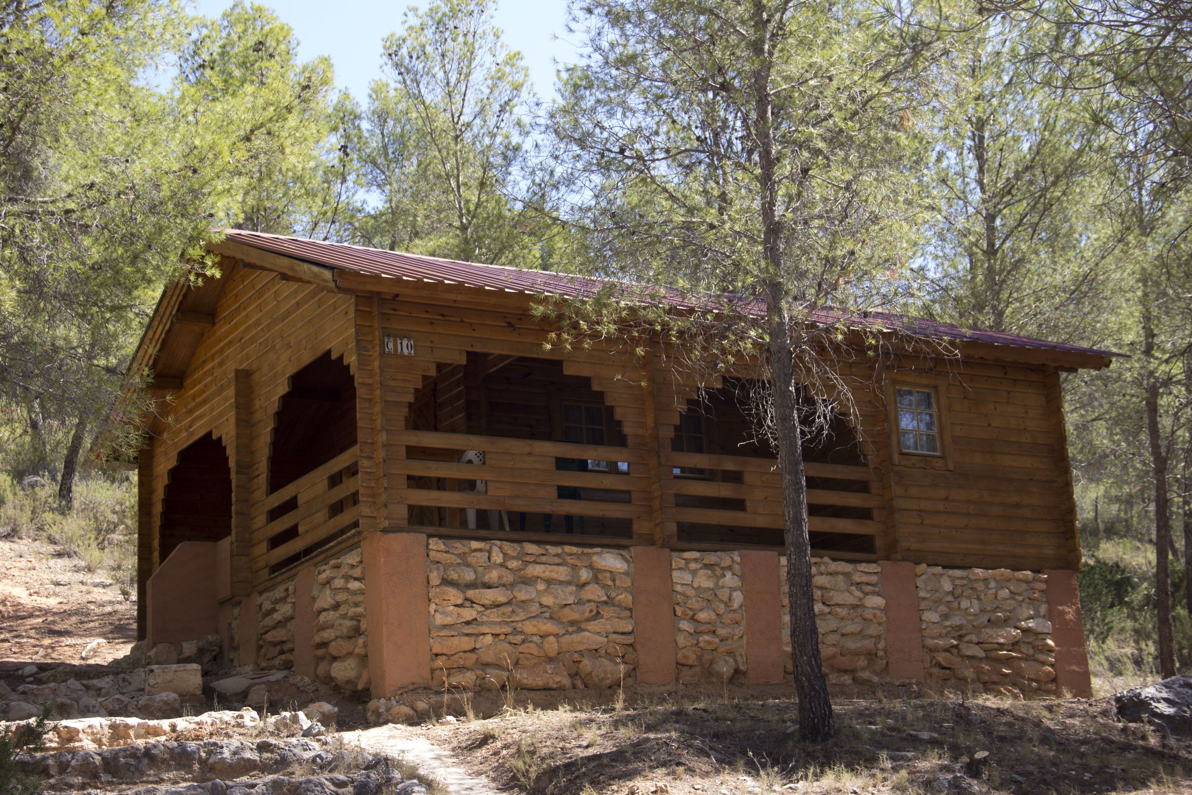 Una cabaña rústica de madera con base de piedra, ventanas amplias y un porche cubierto.