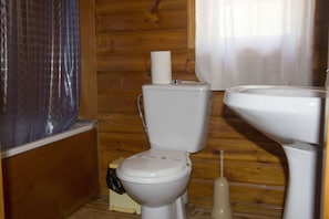 A small, compact bathroom with a wooden interior, a toilet, a sink, and a shower curtain. - Camping La Puerta (Moratalla)