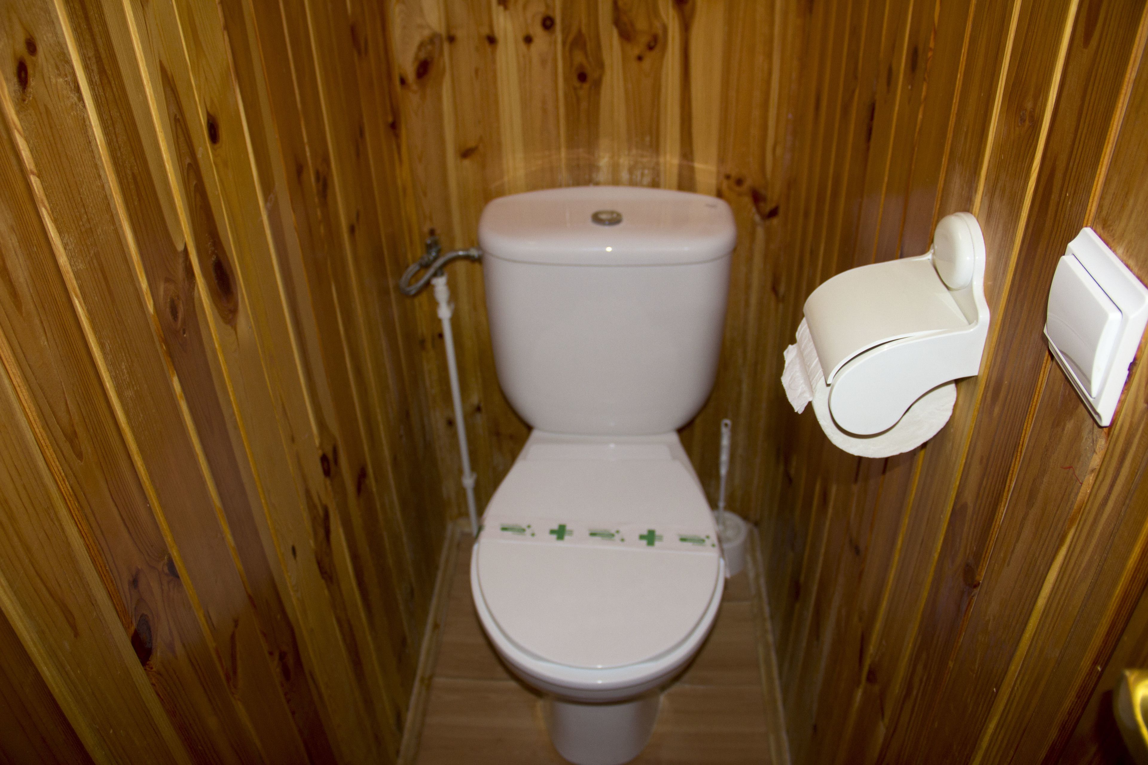 A wooden-paneled bathroom with a white toilet, a wall-mounted bidet, and a toilet paper holder.