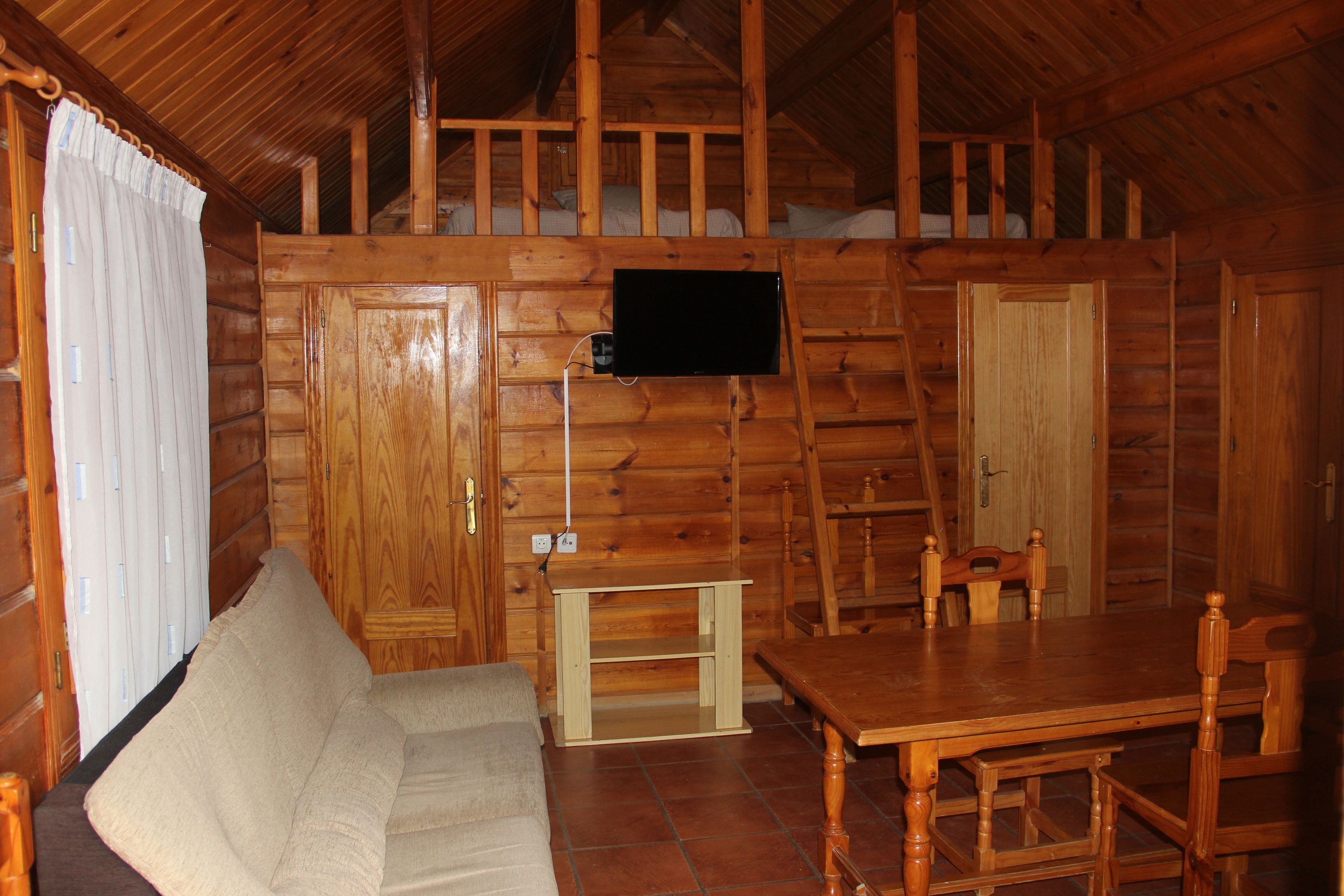 Ein Interieur einer Blockhütte mit einem Holzespeisesaal, Stühlen, einer Couch und einem an der Wand montierten Flachbildfernseher.
